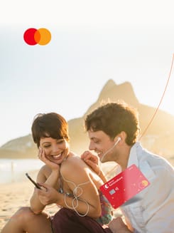 Junges Paar am Strand nutzt Smartphone mit Bankkarte der GLKB für mobiles Bezahlen und Ferienplanung.