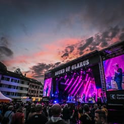 Bühne des Sound of Glarus Festivals bei Sonnenuntergang mit Publikum und Lichtshow im Stadtzentrum.